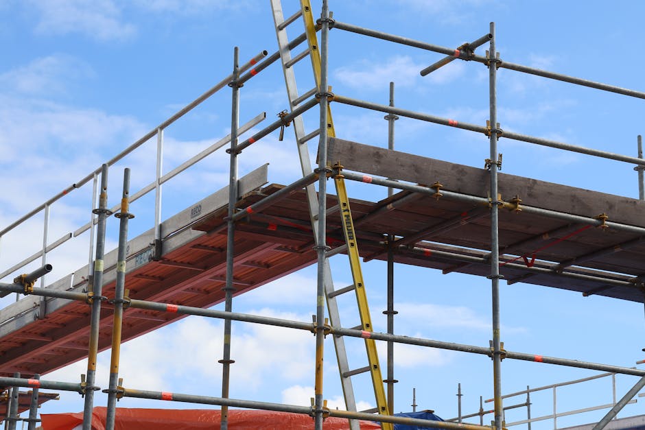 Gedetailleerde weergave van een steigerconstructie en een ladder op een bouwplaats tegen een helderblauwe lucht.