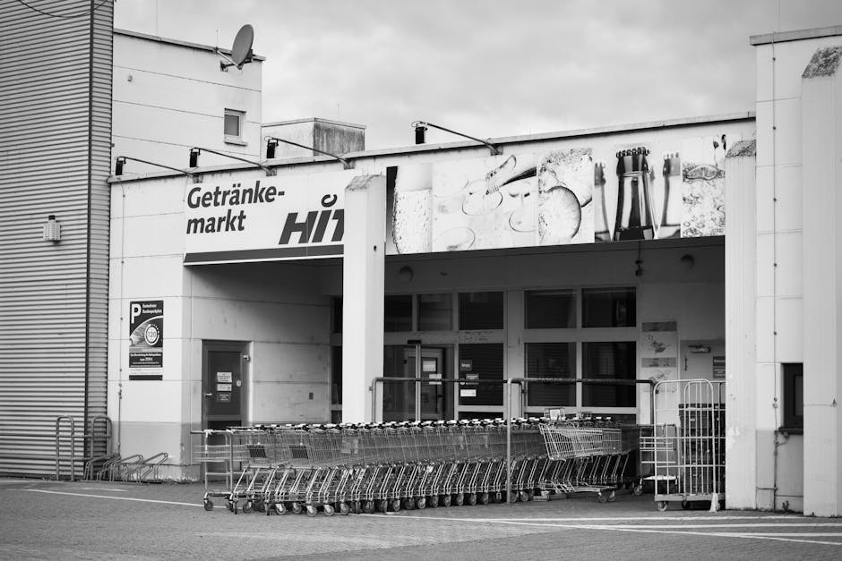 Een zwart-witfoto van de ingang van een supermarkt met een rij winkelwagens.